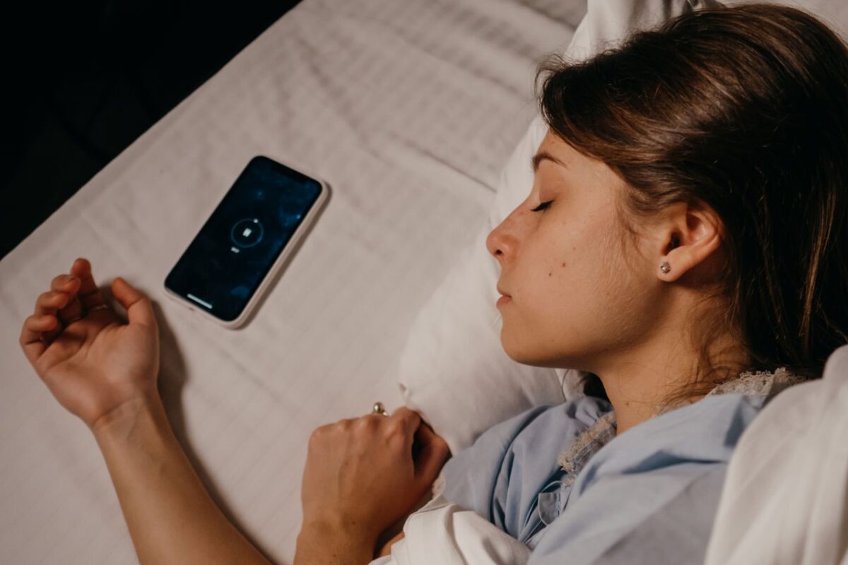 Cozy dark bedroom with a phone playing calm sleep music on a nightstand
